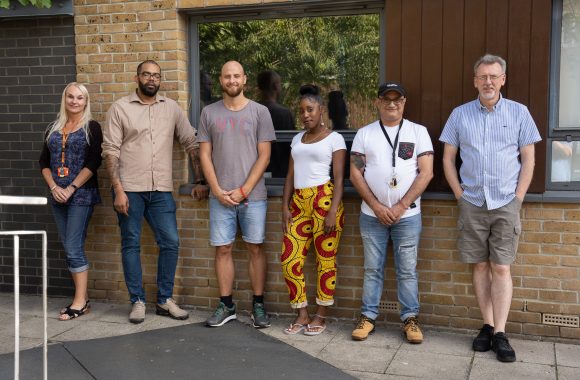 six people standing outside a building in a row smiling at the camera