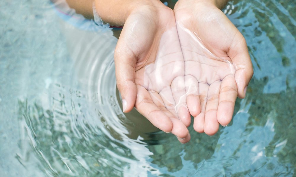 Hands cupping clear water from a spring